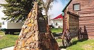 A large stone monument is located in front of a log cabin. AI generated content